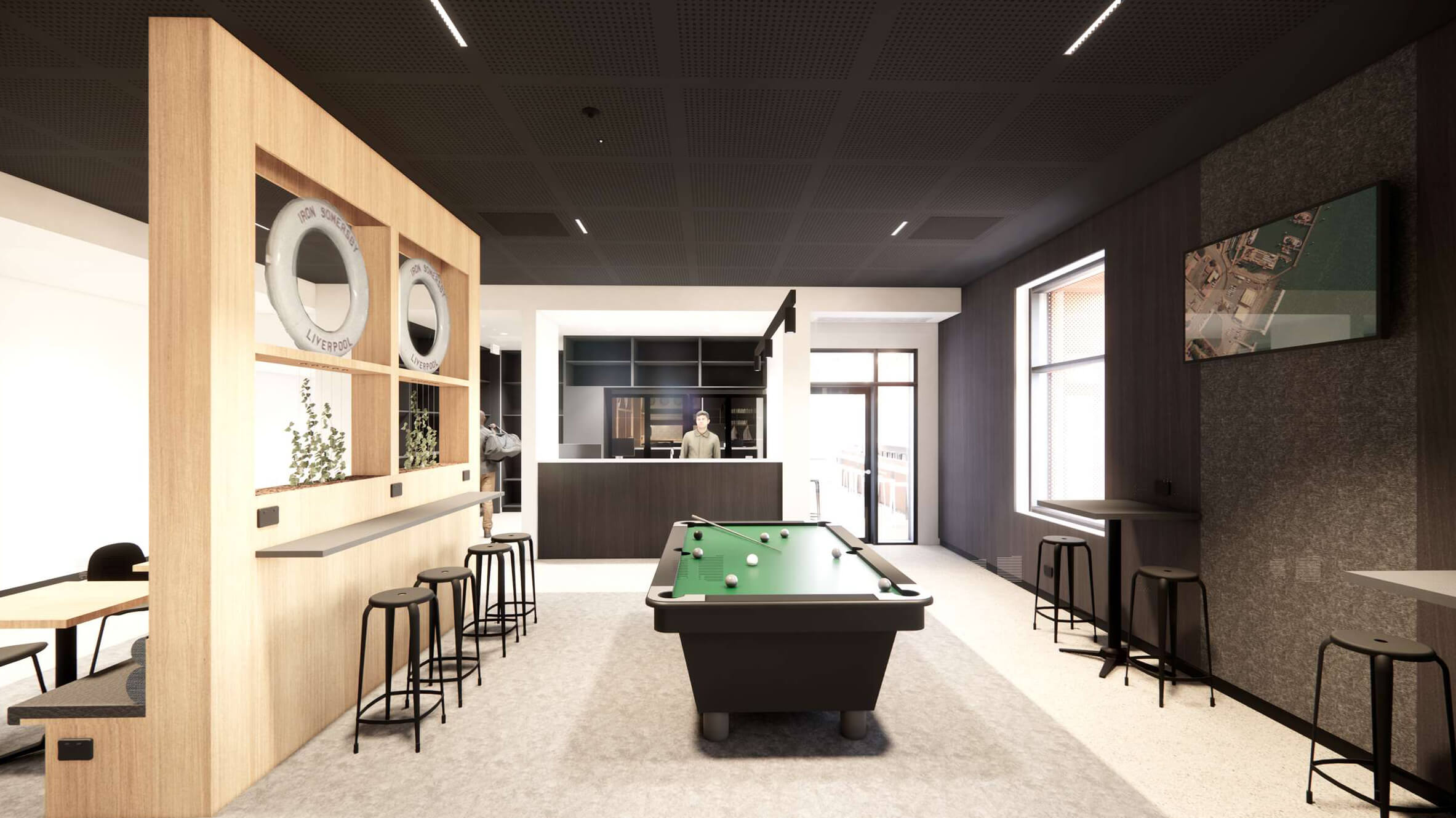Modern recreation room with a pool table centered, high stools along wooden partition and bar counter, a man standing behind the reception desk, and a TV mounted on the wall.